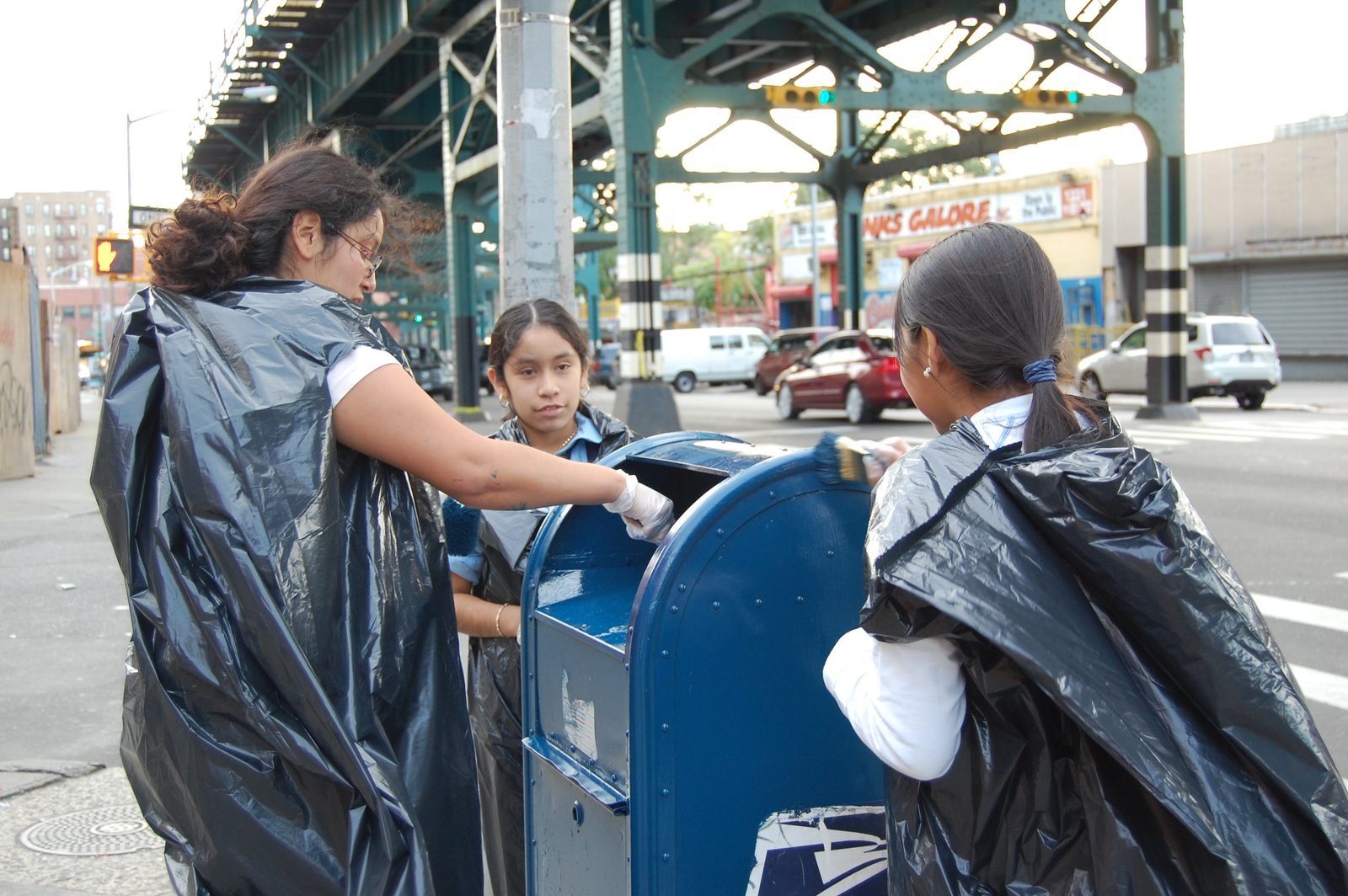 Mentees covering a blue street mailbox with plastic sheeting before painting it.
