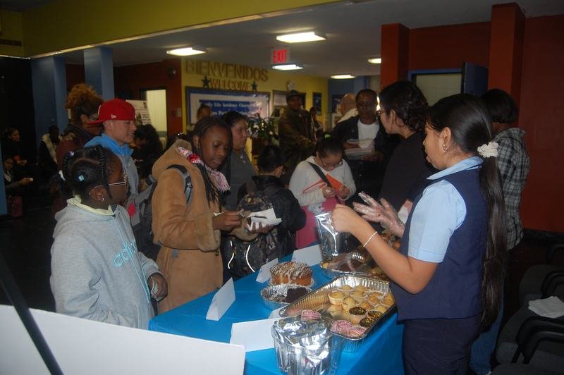 Families crowding around a long bake sale table covered in wrapped baked goods.