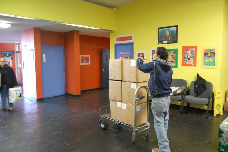 Cardboard donation boxes stacked on a hand truck in a programme hallway.