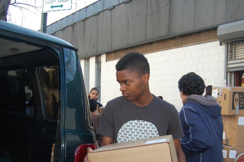 A boy carries a cardboard donation box towards the open back of a van.
