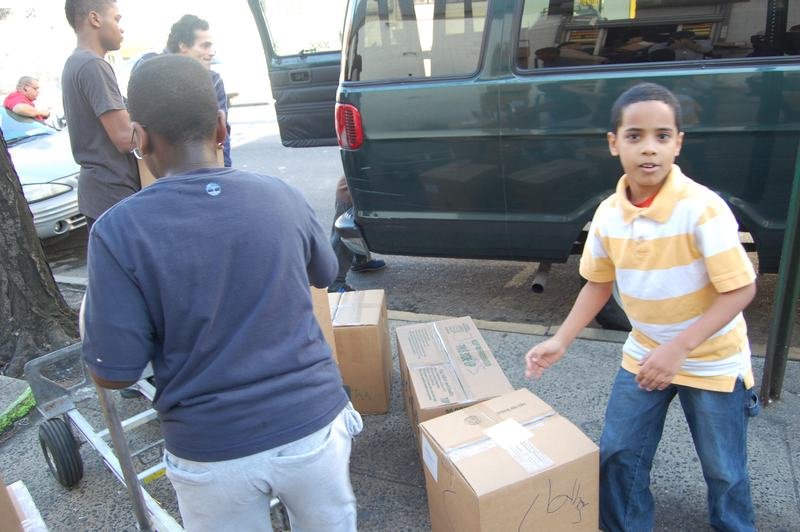 Two boys carrying cardboard boxes to a van during a donation drive.
