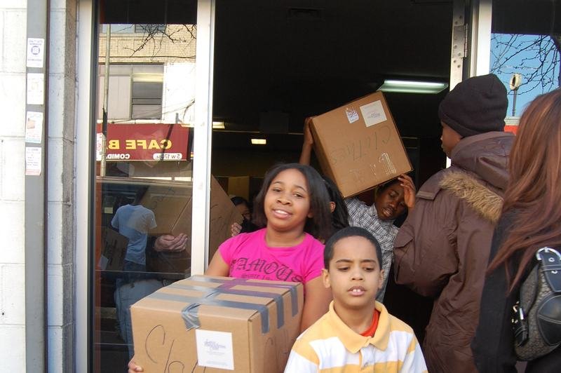 Mentees carrying donation boxes and packs of bottled water out through a doorway.