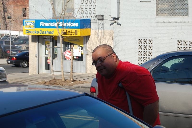 A volunteer in a red shirt leans on a car door on a Bronx street during a donation run.