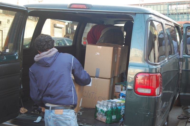 A volunteer loading marked cardboard boxes and bottled water into the back of a van.
