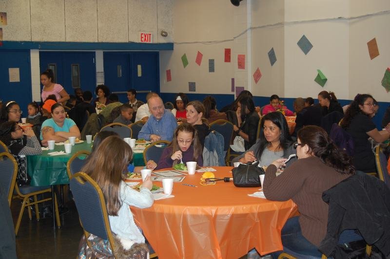 Families seated at round tables with orange and green cloths at a BOOM family event.