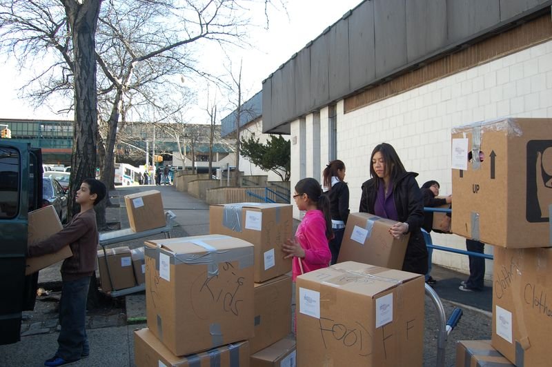 Volunteers and mentees stacking donated food boxes on a Bronx street.