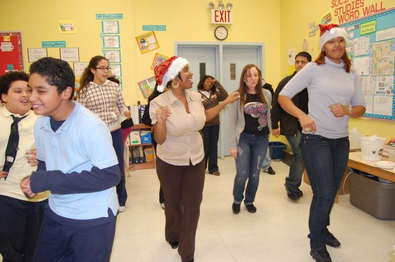 Mentors and mentees dancing together in a classroom decorated for the holidays.