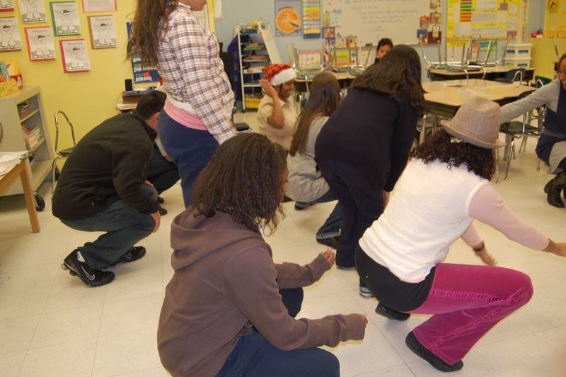 Mentors and mentees crouching on a classroom floor during a holiday party game.