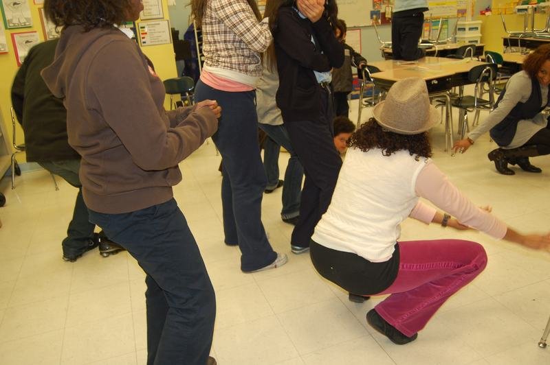 A mentee dancing low to the floor while others watch at a classroom holiday party.