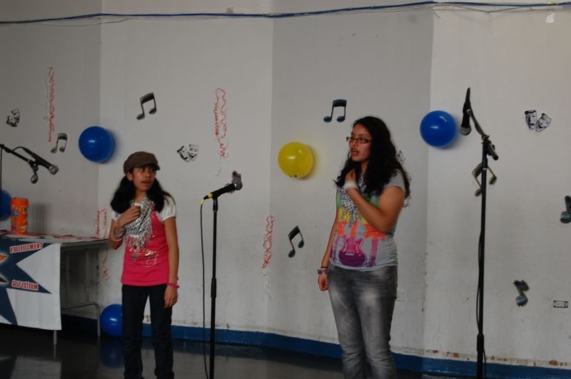 Two mentees singing at microphones in front of a wall decorated with paper music notes.
