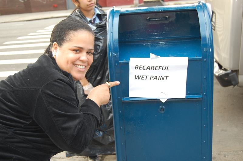 A volunteer points to a hand-written wet paint sign taped to a freshly painted mailbox.